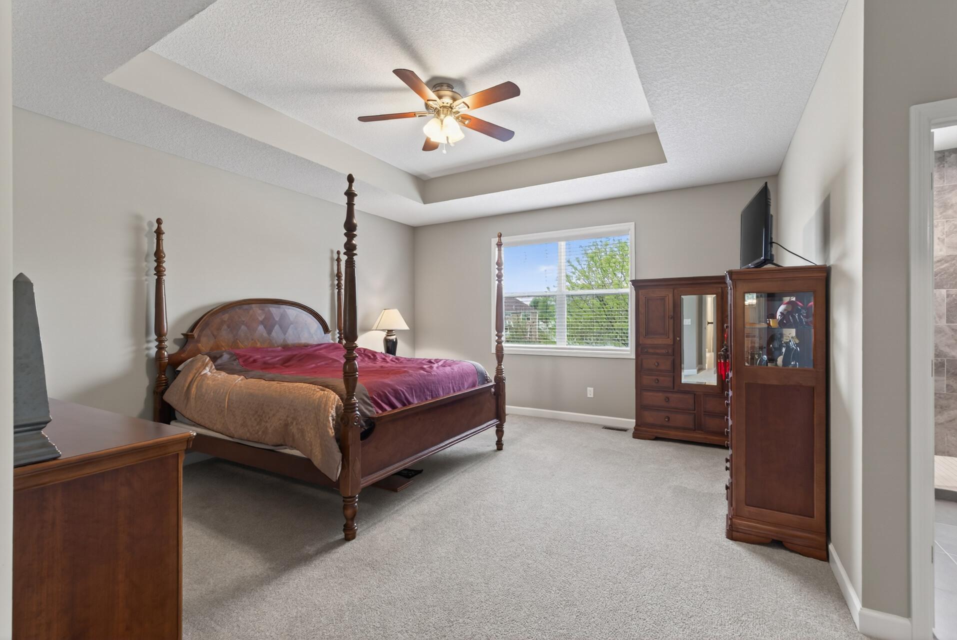 The primary bedroom is truly a private retreat with a tray ceiling, abundant natural light, and a ceiling fan.