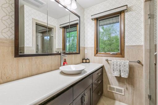 The bath has a long vanity with a vessel sink, ceramic wall tile and tile flooring, and a tile shower.