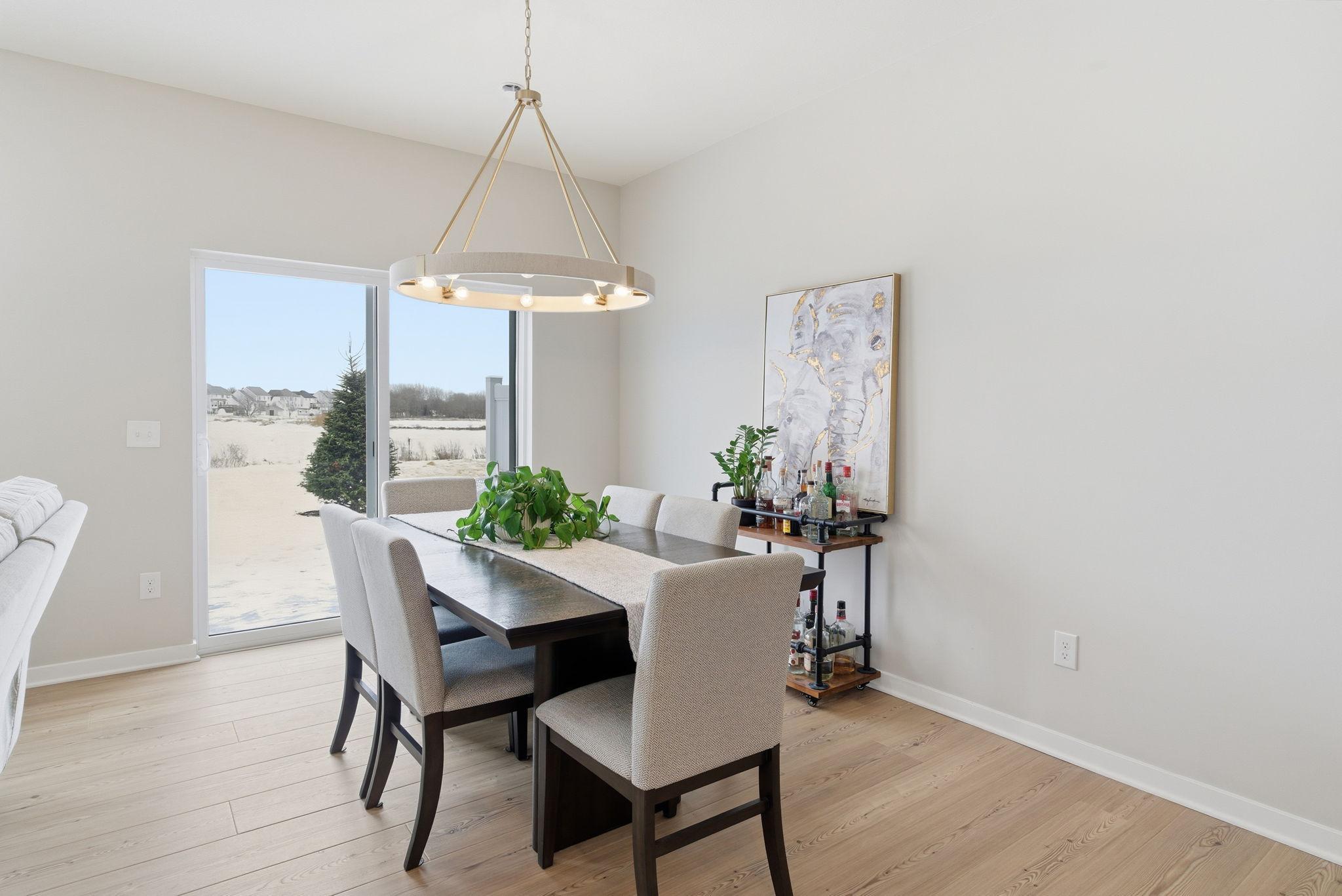 A sunlit dining space features a sliding glass door with outdoor access to your patio. Designer lighting creates a perfect backdrop for family meals & special gatherings, adding warmth and character to the space while enhancing the overall ambiance.