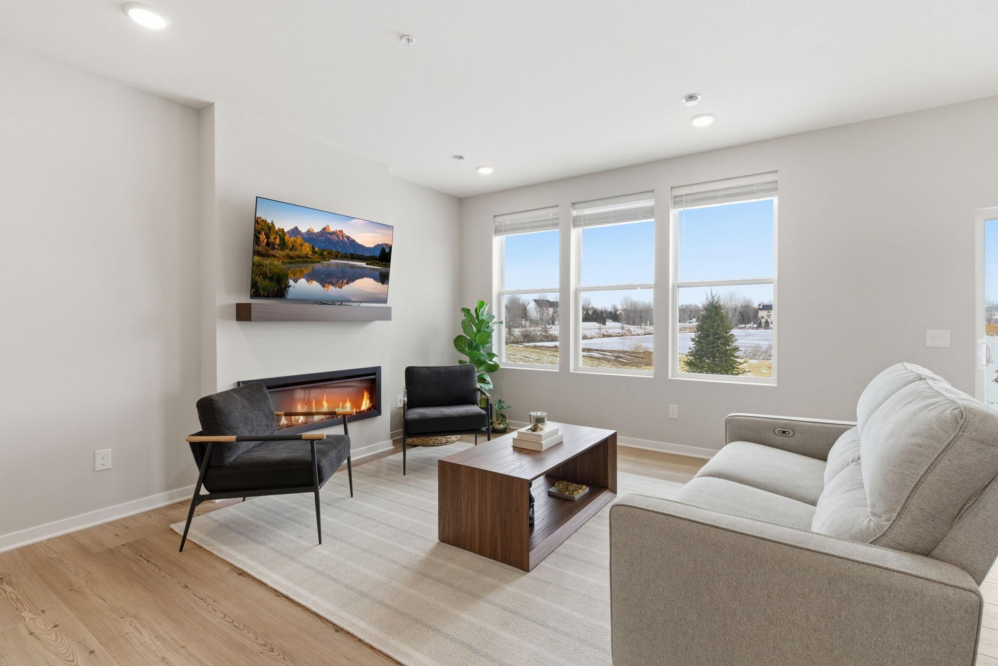Enjoy an elegant open-concept living space designed for refined modern living, anchored by a long sleek electric fireplace adding warmth & architectural interest. Three side-by-side windows frame serene pond views, filling the room with natural light