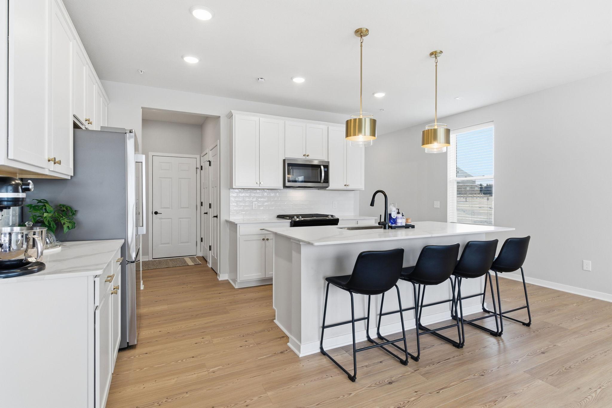 High-end stainless steel appliances including a gas range, custom subway tile backsplash, and statement pendant lighting create a sophisticated yet inviting atmosphere.