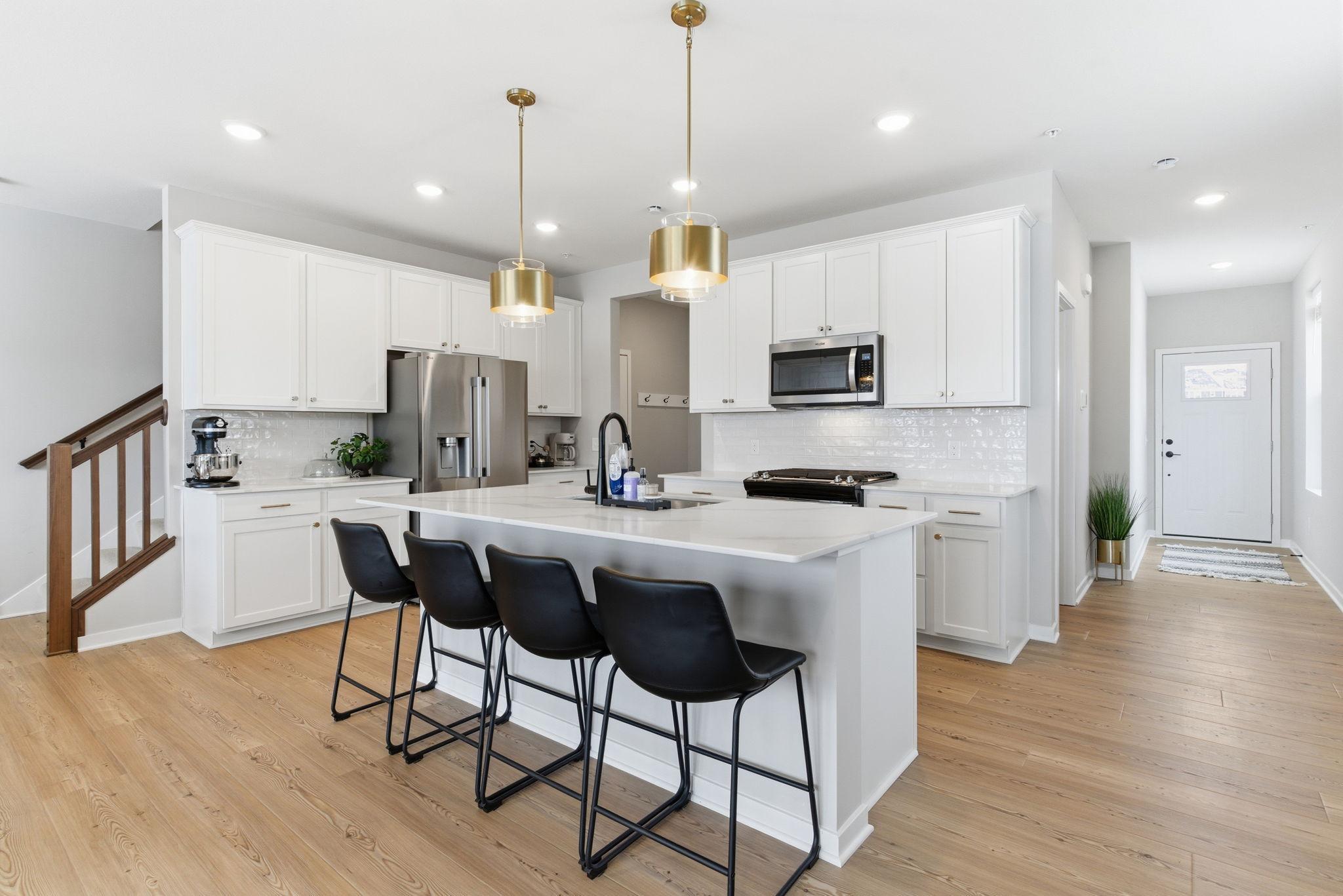 A stunning chef’s kitchen showcasing refined modern design and exceptional craftsmanship. Pristine white cabinetry, expansive quartz countertops, and an oversized waterfall island with designer seating anchor the space.