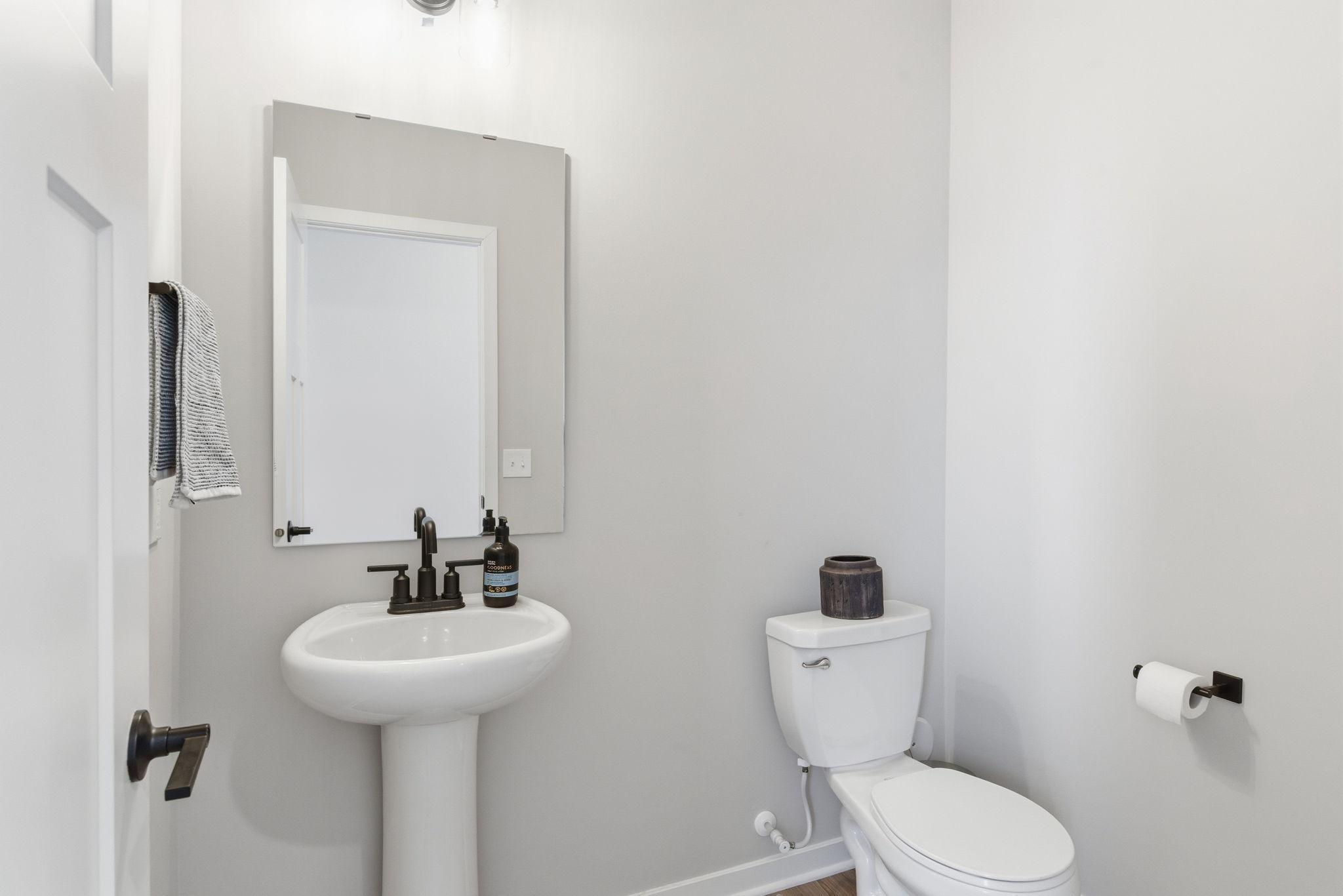 An elegant main-level powder room features a classic pedestal sink paired with rich black fixtures. Soft neutral tones and refined finishes create a polished, timeless look—perfect for guest convenience.