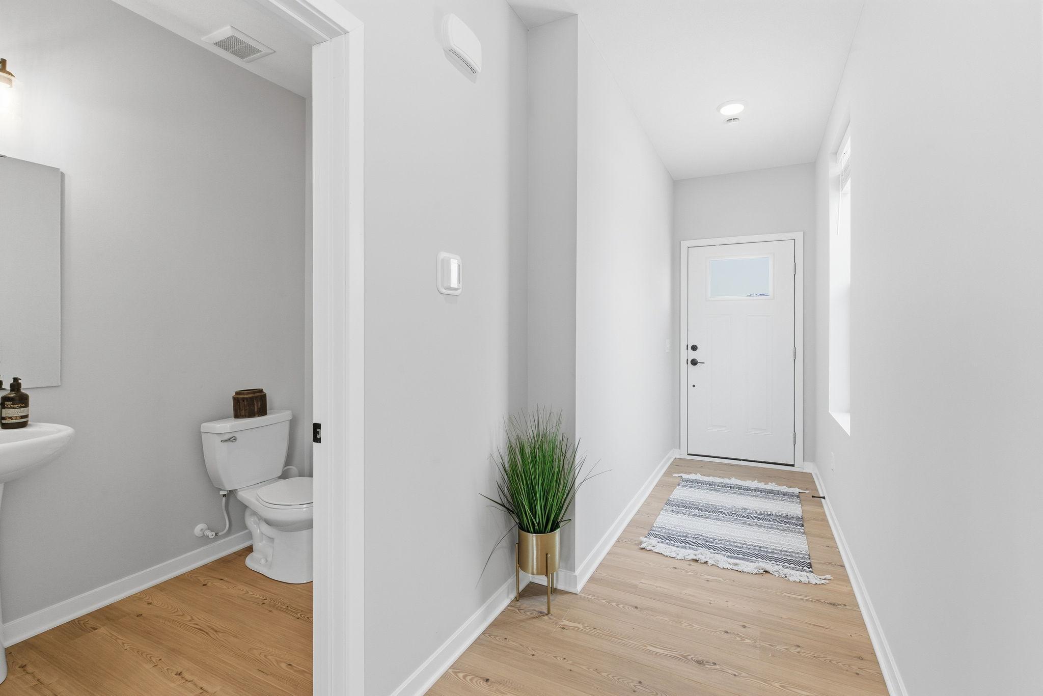 A welcoming front hallway is highlighted by soaring ceilings, crisp white trim, & soft neutral walls that create an airy, refined first impression. Natural light streams through the window, enhancing the sense of openness & showcasing the home.