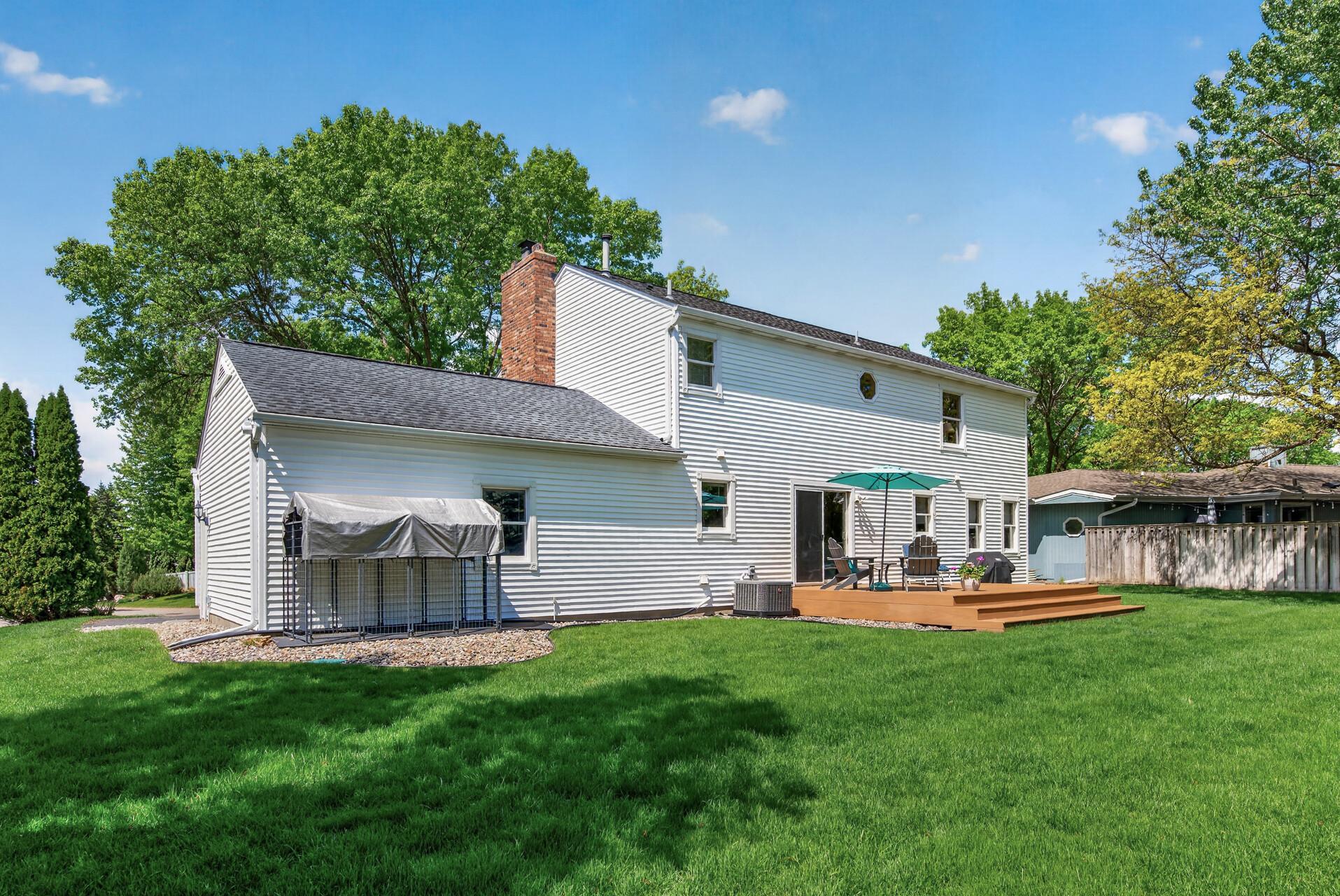 Rear exterior showcases generous green space, oversized deck, and beautifully maintained grounds