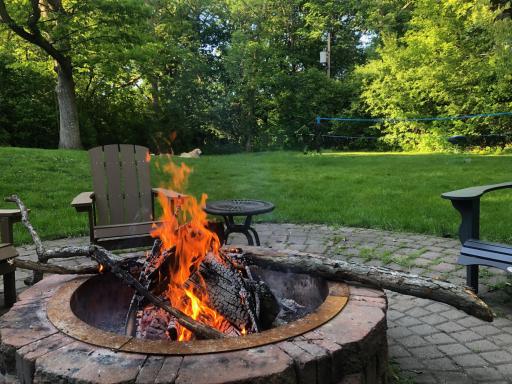 Ready for sâmores? This view from the paver patio showcases the built-in fire pit and lush wooded views. A seamless extension of the walk-out lower level, this space is designed for entertaining friends and enjoying nature in total privacy.