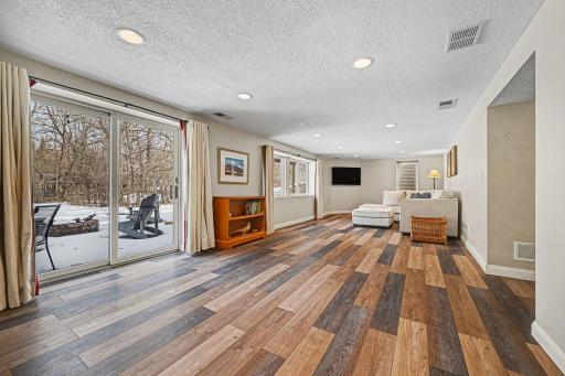 Bright and airy walk-out level! Enjoy LVT plank floors & modern knock-down ceiling with recessed lights. The patio door leads directly to a fire pit and paver patio, blending indoor comfort with outdoor fun. A versatile space for relaxing or hosting.