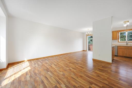 A wider look across the living and dining areas, with sunlight pouring in and the kitchen and deck just beyond