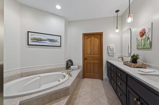 Private primary bath featuring dual vanities, soaking tub, and tiled flooring.