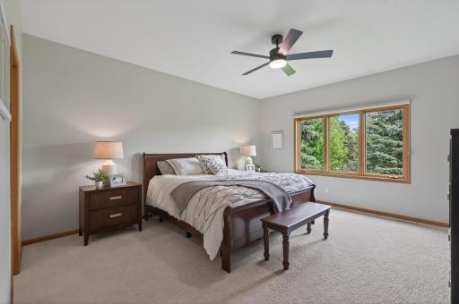 Spacious primary bedroom with plush carpet and oversized windows overlooking mature trees.