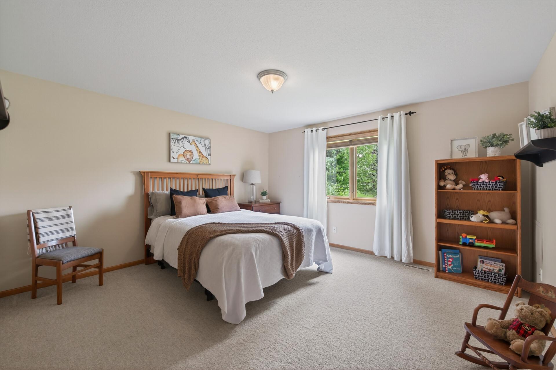 Spacious upper-level bedroom with neutral finishes, large window, and generous floor space.