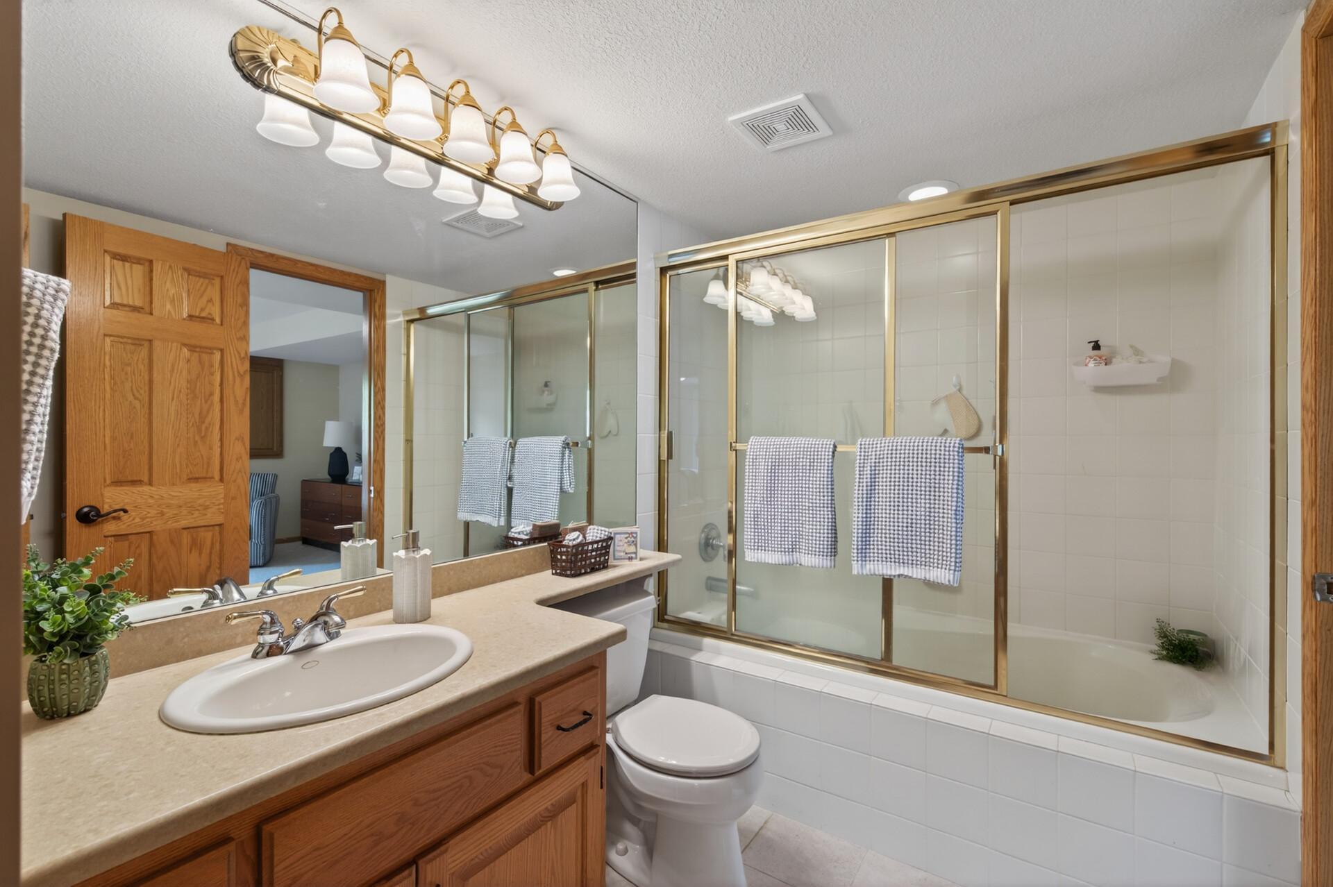 Full lower level bath with oversized vanity, tiled tub surround, and abundant storage space.
