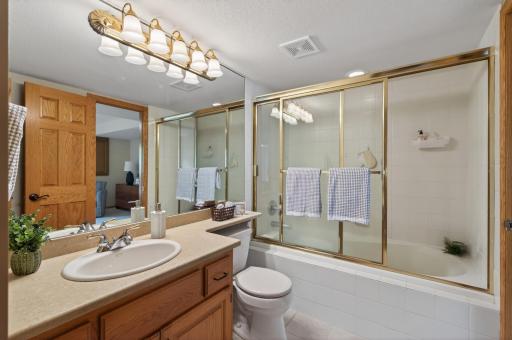 Full lower level bath with oversized vanity, tiled tub surround, and abundant storage space.