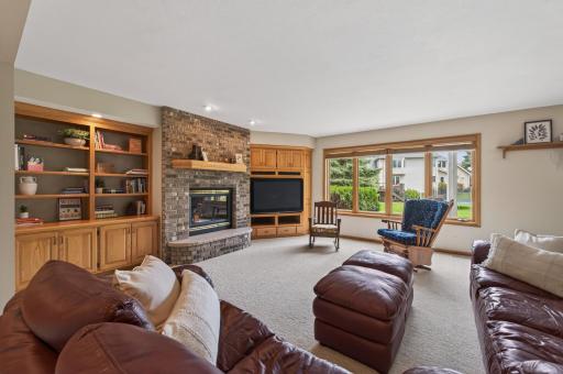 Cozy lower-level family room featuring brick fireplace, built-ins, and scenic backyard views.