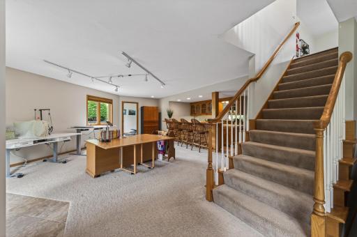 Open lower-level recreation space with wet bar, staircase access, and flexible hobby/work areas.