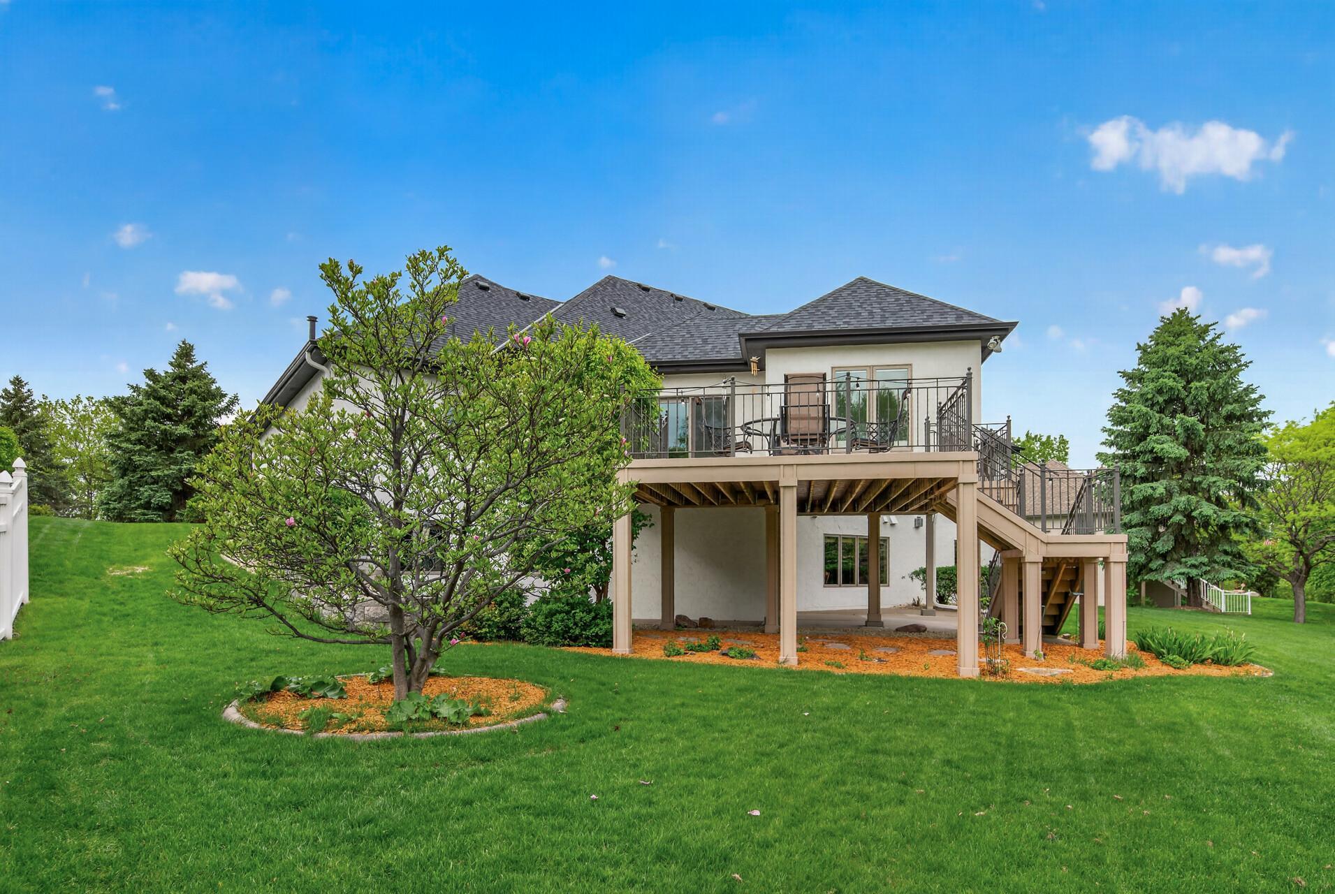 Spacious backyard with mature landscaping, open green space, and under-deck patio area.