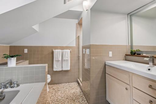 Second-floor full bath with a wood vanity, tiled tub surround, glass shower, and classic mosaic tile flooring.
