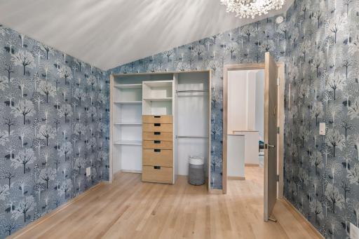 Spacious bedroom with custom built-in wardrobe, hardwood floors, and distinctive woodland-inspired wallpaper.