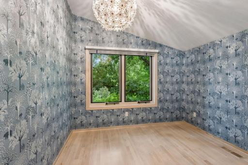Light-filled bedroom with vaulted ceiling, beautiful woodland wallpaper, and serene treetop views.