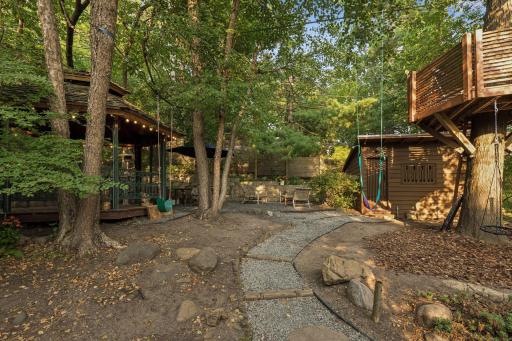 Private wooded oasis with winding paths, mature trees, stone landscaping, and multiple inviting spaces for outdoor relaxation and play.