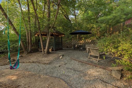 Secluded wooded setting with a charming screened gazebo, outdoor dining area, stone retaining walls, and a fun hanging swing.