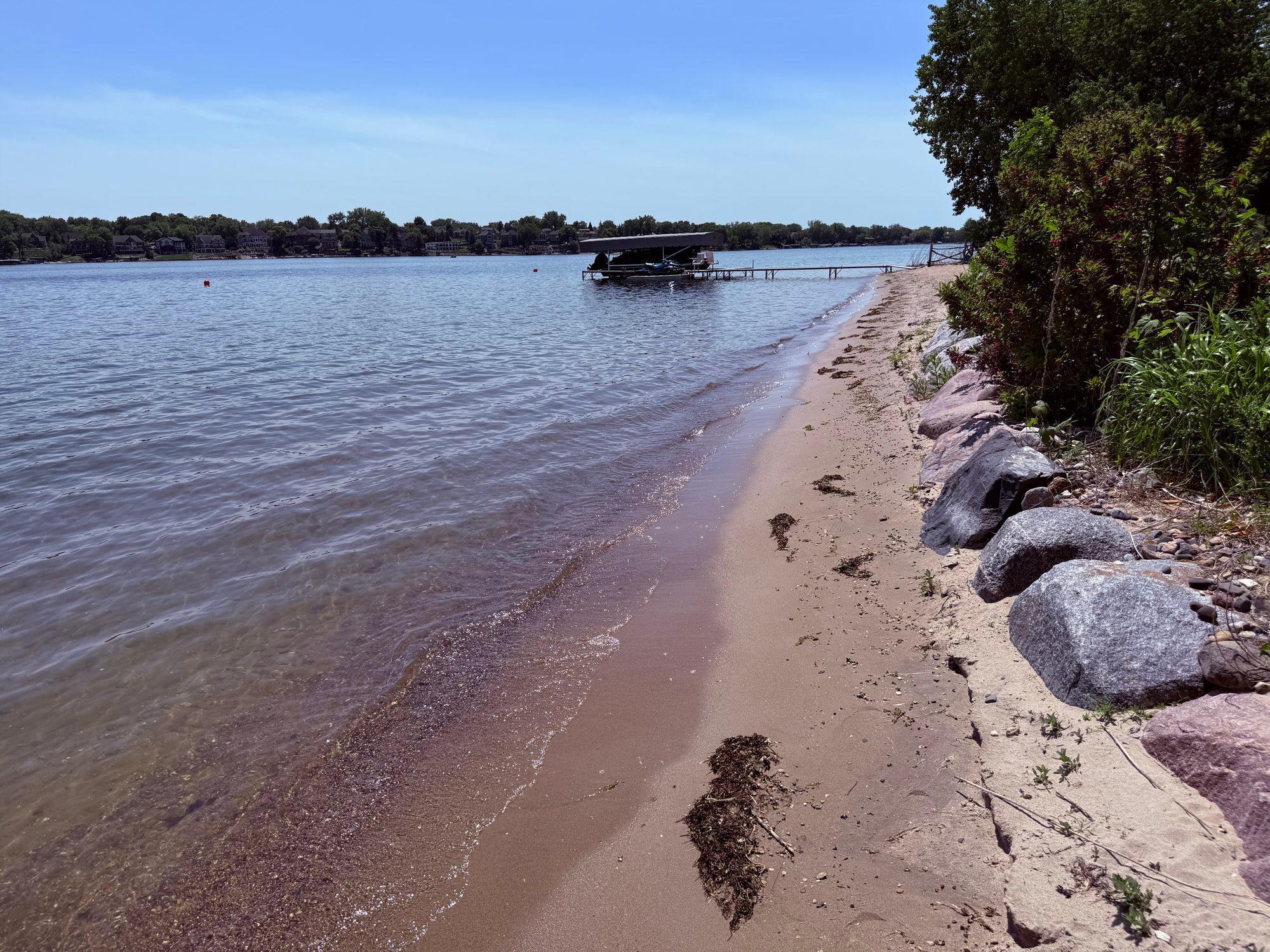 Sandy shoreline and large rip rap boulders. View to the west