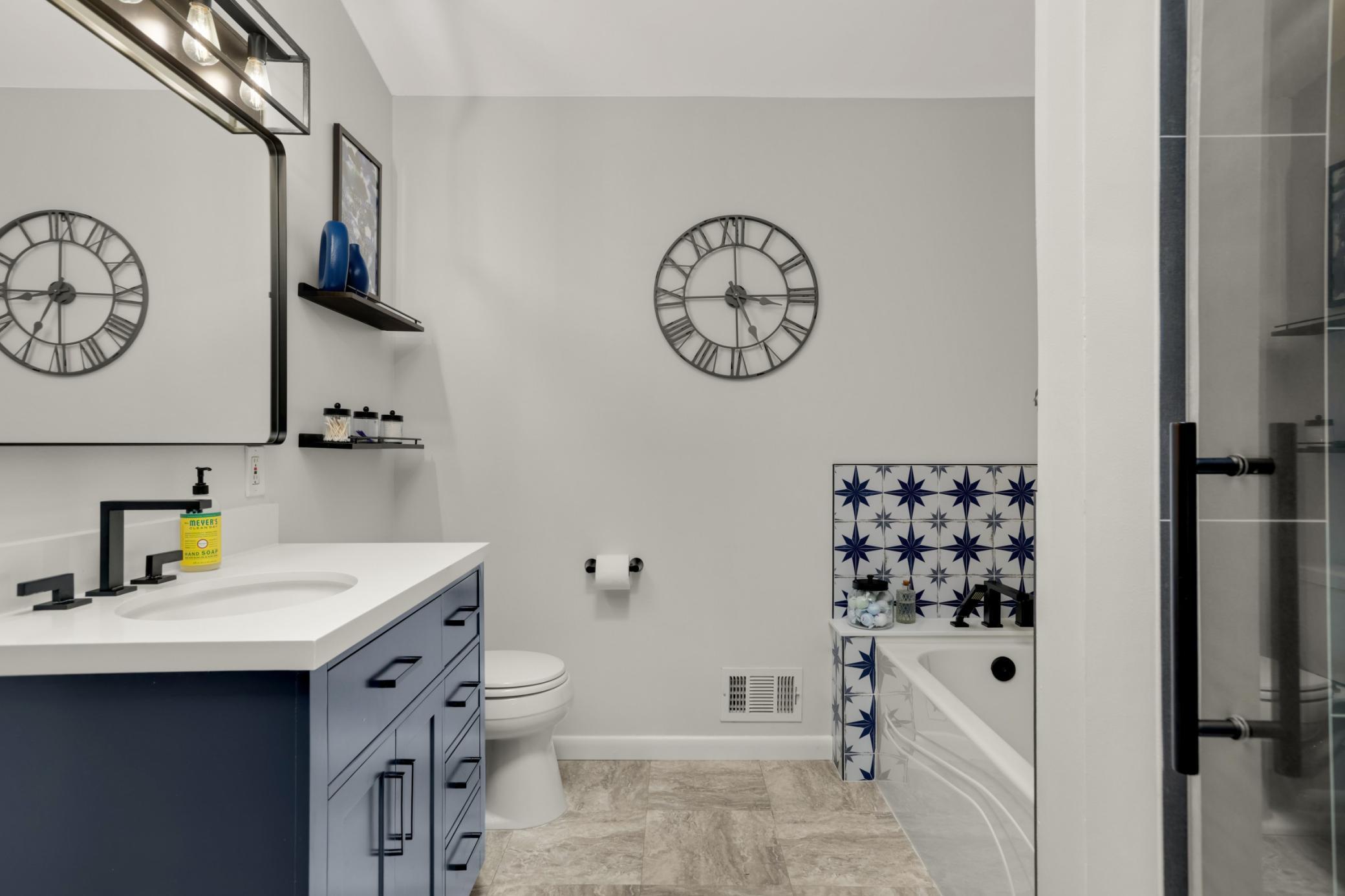 This beautifully remodeled bathroom blends modern design with spa-like comfort. The updated vanity showcases rich navy cabinetry, quartz-style countertops, matte black hardware, and modern lighting for a sophisticated touch.