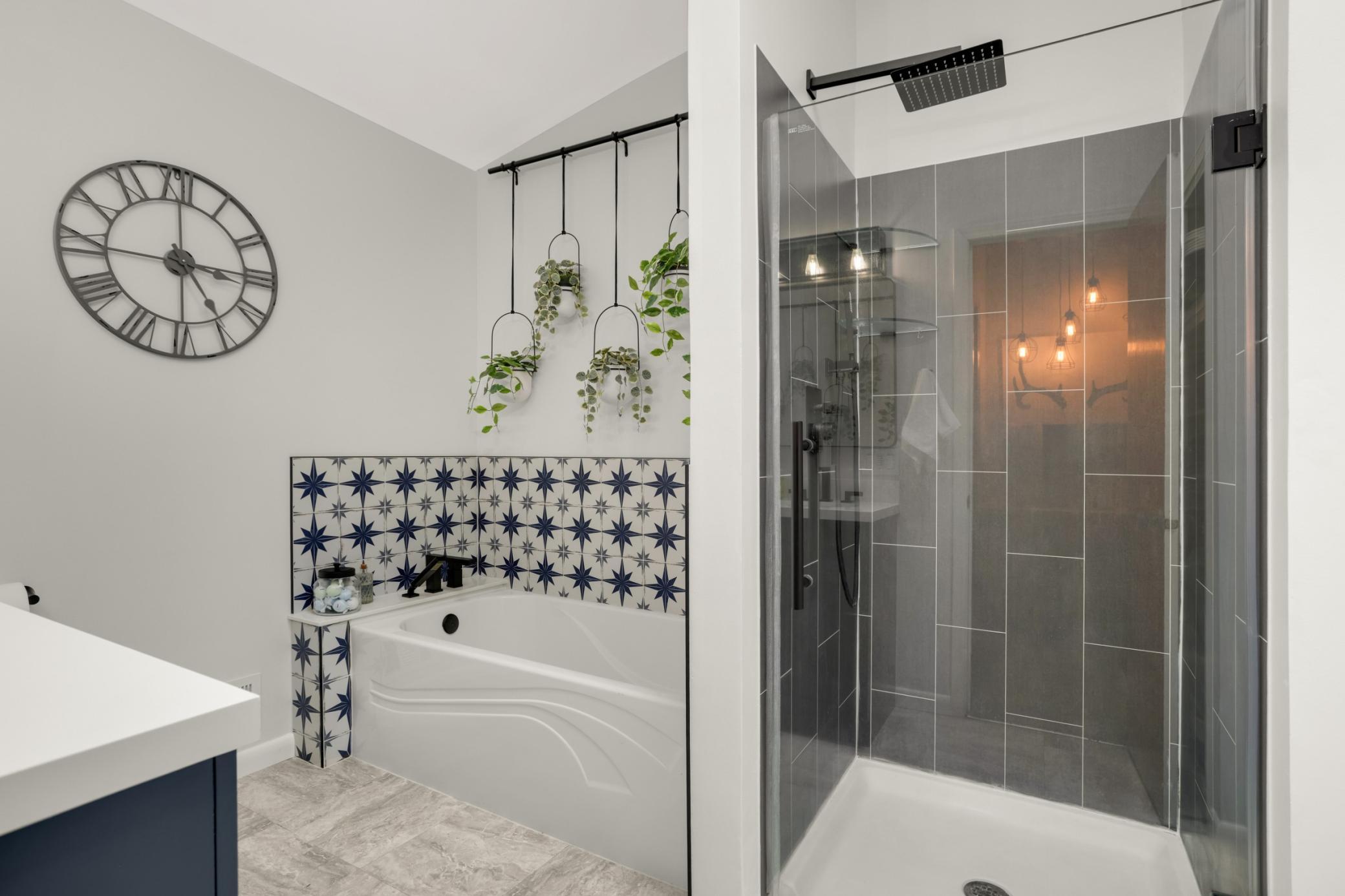 Featuring a stunning walk-in glass shower with sleek black fixtures and large-format gray tile, the space offers a clean and contemporary feel. The separate soaking tub is accented with eye-catching patterned tile, creating a stylish focal point