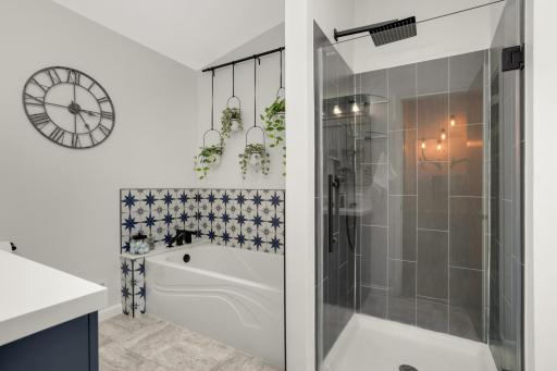 Featuring a stunning walk-in glass shower with sleek black fixtures and large-format gray tile, the space offers a clean and contemporary feel. The separate soaking tub is accented with eye-catching patterned tile, creating a stylish focal point