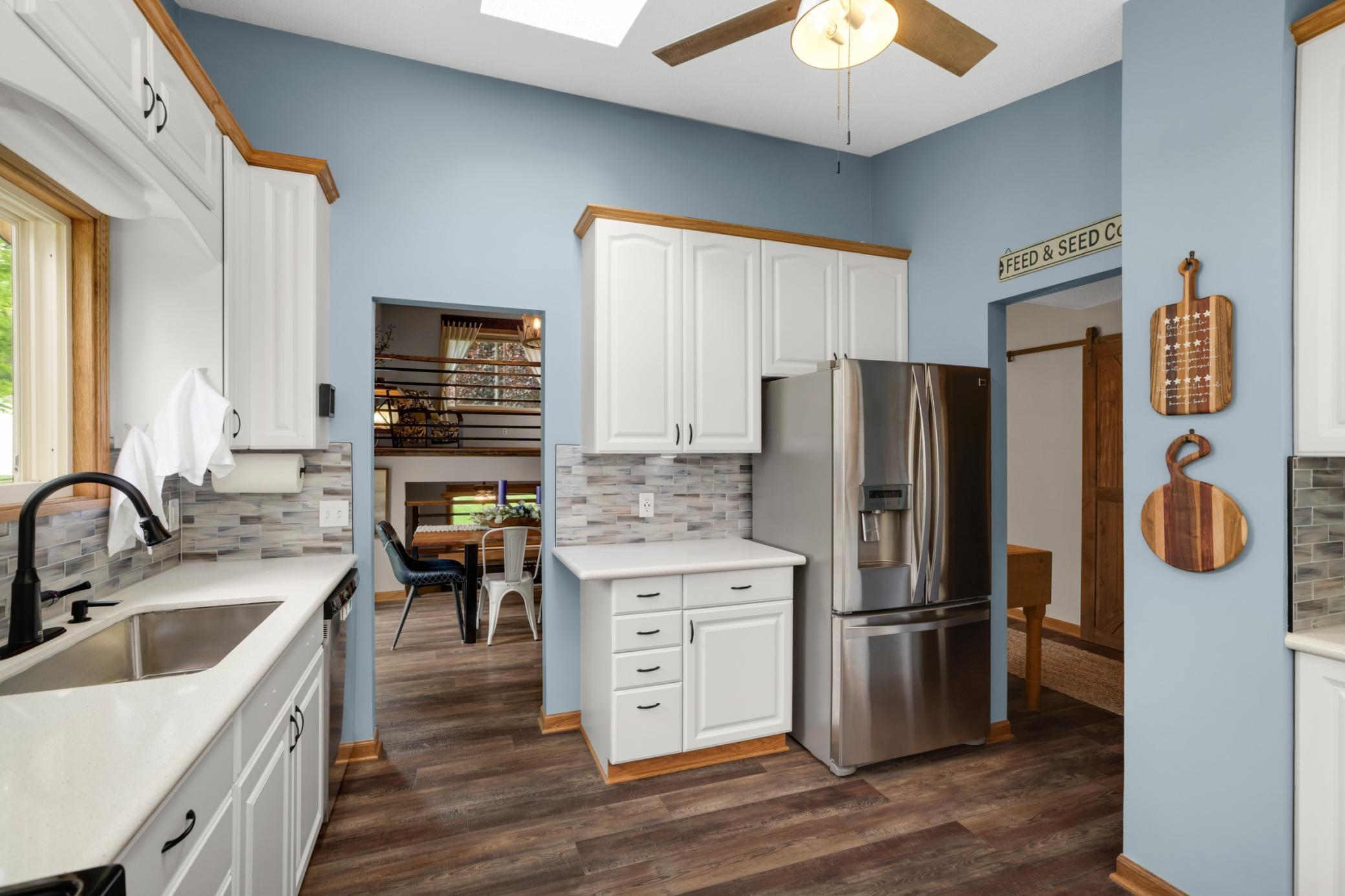 The contemporary tile backsplash & updated black hardware provide a stylish finishing touch throughout the kitchen. The kitchen also features durable updated flooring, a skylight, ceiling fan, & ample cabinetry for storage & organization.