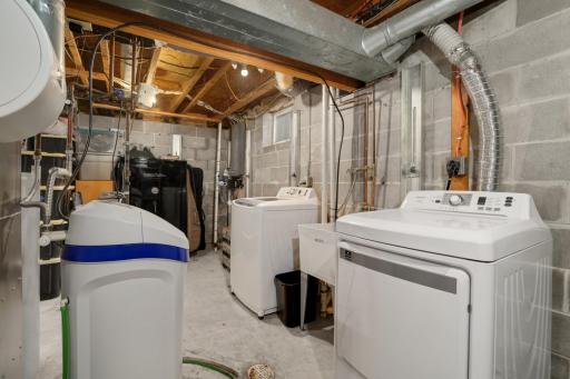 The laundry area is clean and practical, featuring a full-size washer and dryer new in 2021, utility sink access, and additional room for organization and storage and a new water softener in 2024.