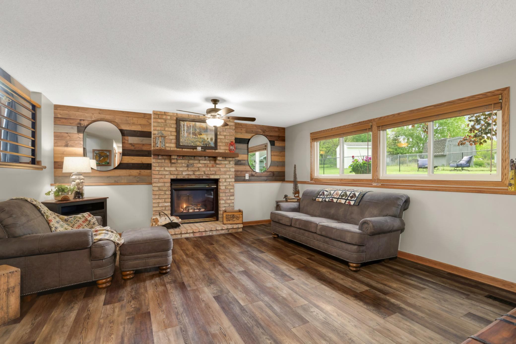 This spacious lower-level family room offers the perfect combination of warmth, comfort, and rustic charm. Centered around a cozy brick gas fireplace with a wood mantel and striking wood accent wall, the space creates an inviting atmosphere