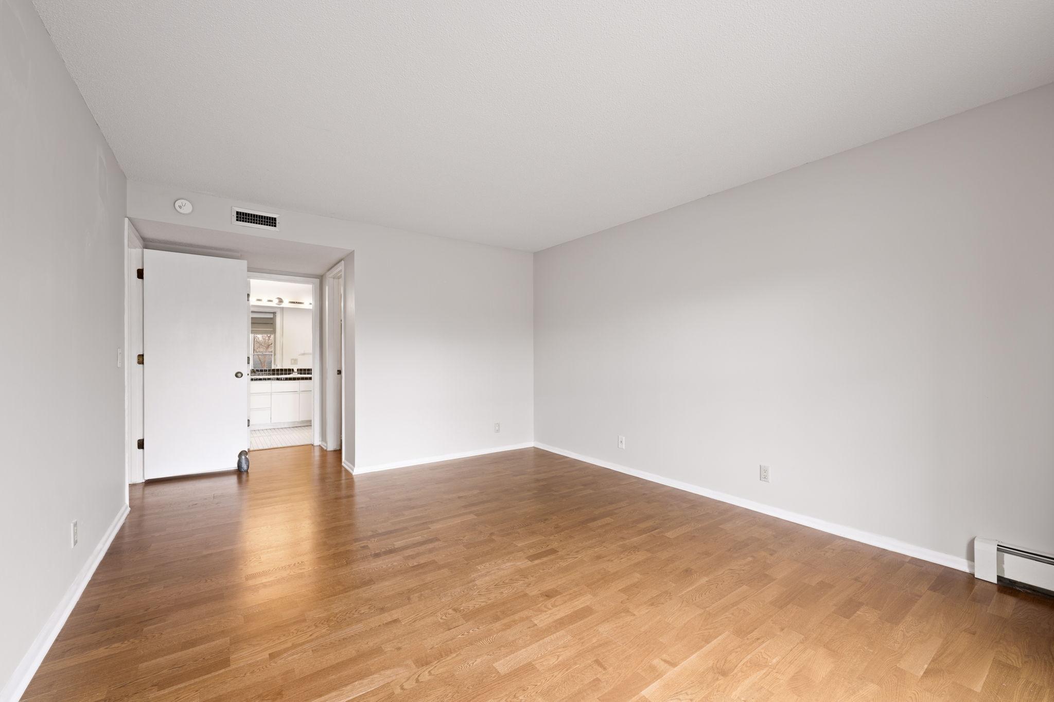 Spacious bedroom with wood-tone flooring and direct access to the nearby bath area.