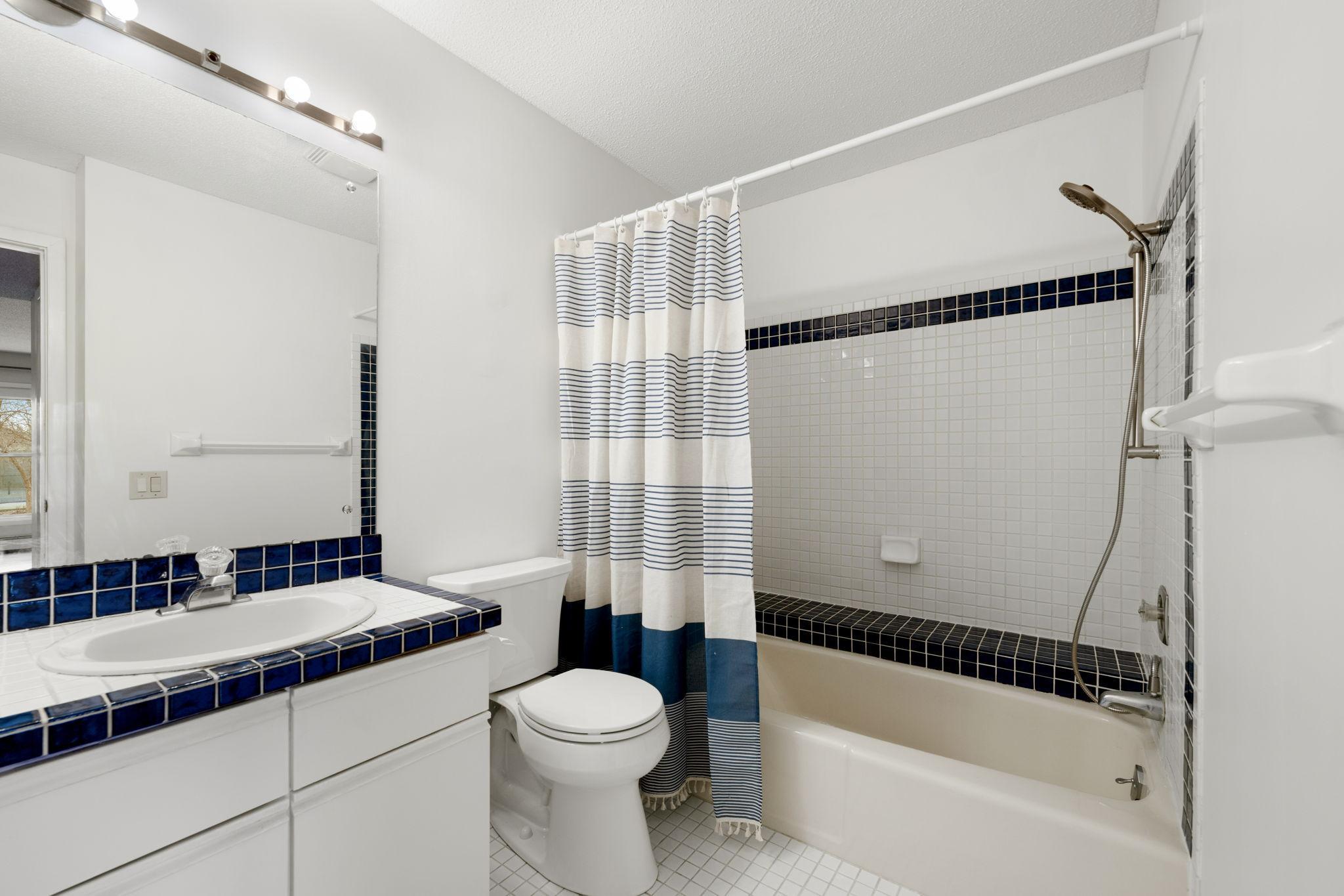 Full bathroom with tiled tub surround, large mirror, and spacious vanity.
