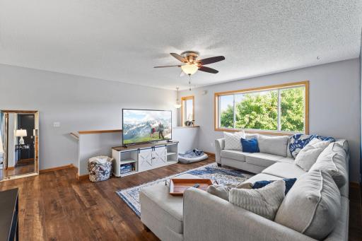 A bright, inviting living room filled with soft natural daylight streaming through large windows. The space feels open and uncluttered, with a seamless flow between seating areas. Light bounces off neutral-toned walls, enhancing the airy atmosphere.