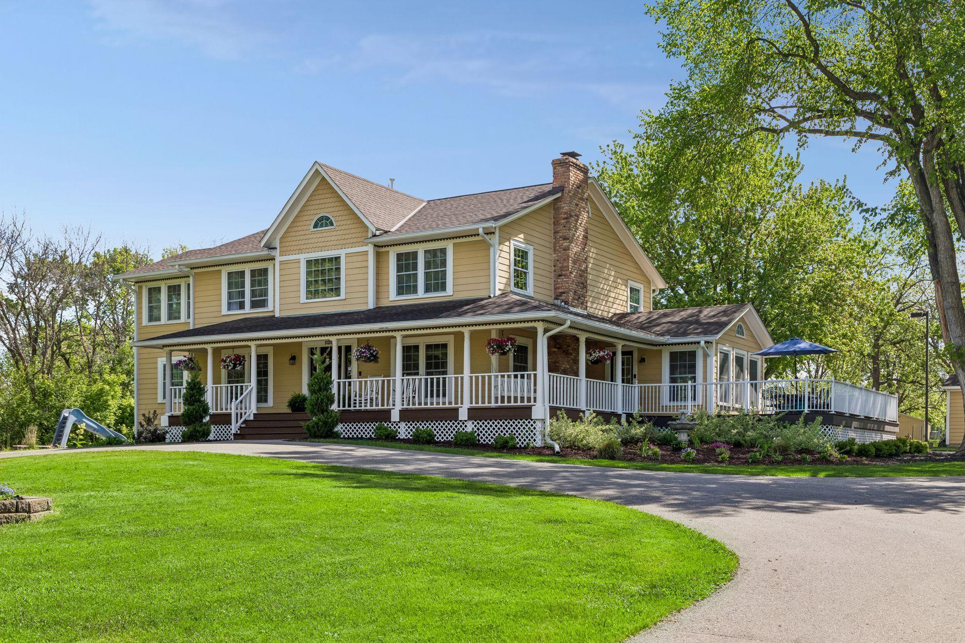 The front circular drive has a flagpole and garden bed. Landscaped beds surround the porch and decks. To the left you can see the pool slide.
