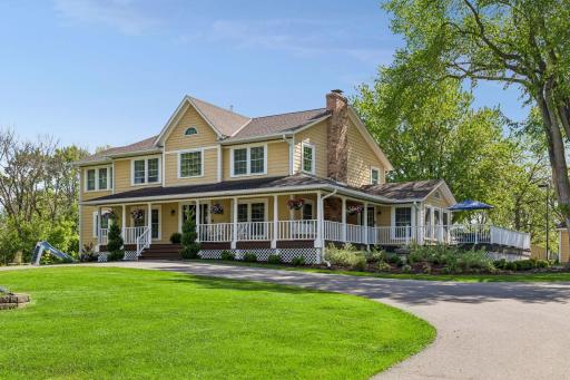 The front circular drive features a flagpole and garden bed, while landscaped beds surround the porch and decks. A pool slide is visible to the left.