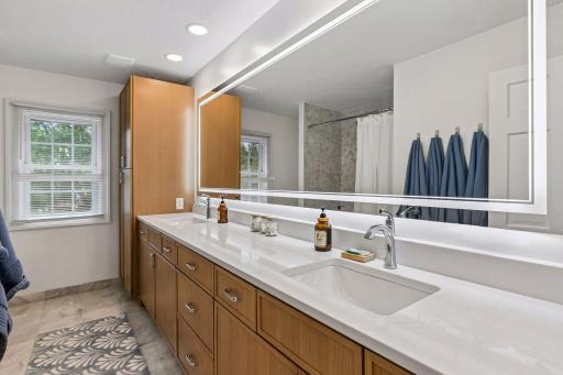 The recently updated second-floor bath features a long quartz dual-sink vanity, a framed LED mirror, and plentiful storage, along with a tiled tub/shower surround and ceramic tile flooring.