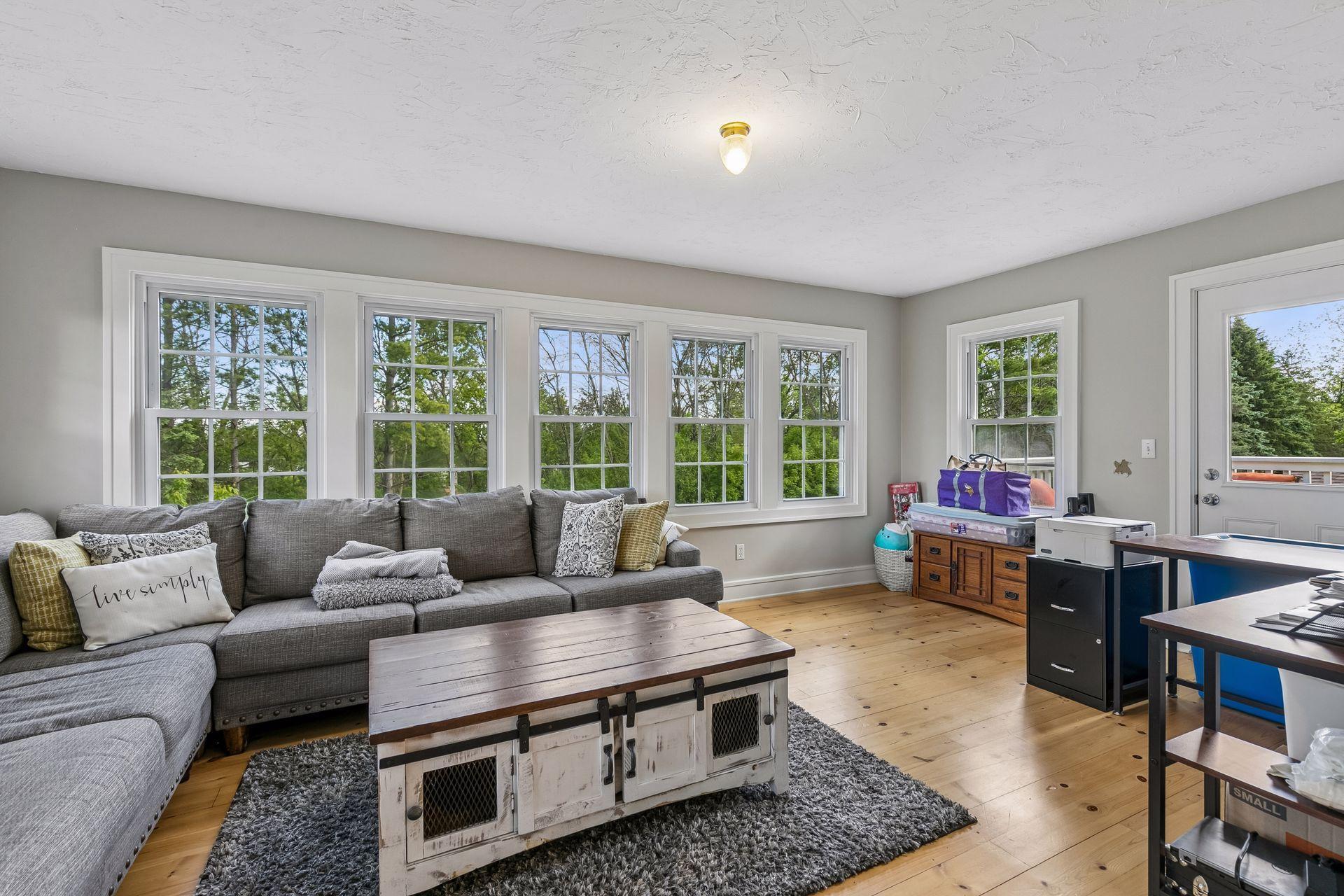 The sitting room has large banks of windows and pine flooring. The door to the right goes out to the upper level deck.