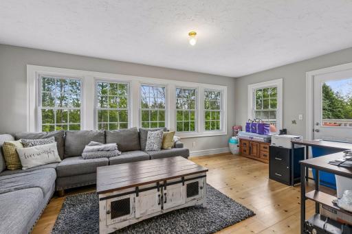 The sitting room features expansive banks of windows and pine flooring, with a door to the right leading to the upper-level deck.