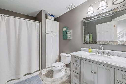 The lower-level bathroom offers an oversized shower, a linen cabinet, and tile flooring.
