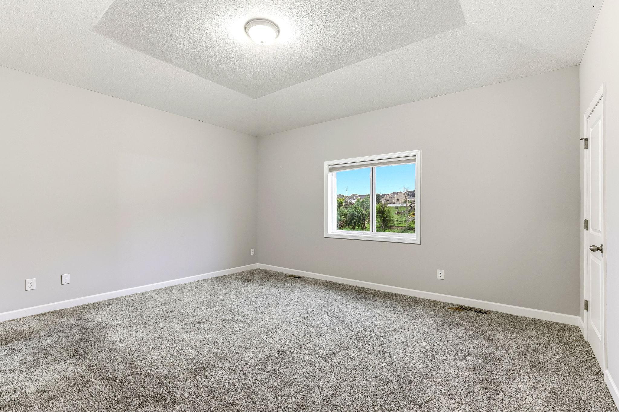 A spacious, serene primary suite highlighted by a beautiful tray ceiling that adds depth, dimension, and an upscale architectural touch.