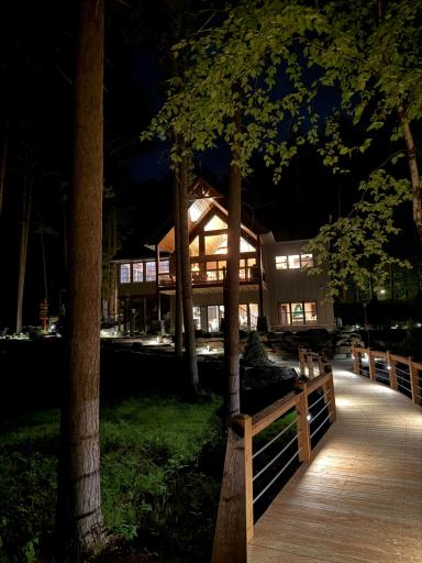 Welcome home day or night—beautifully illuminated walkway leads to a warm and inviting lakeside retreat.