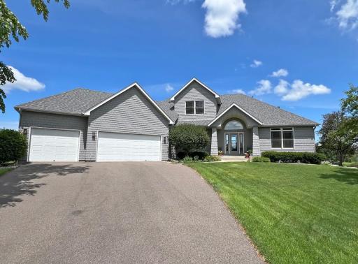 Wide front exterior view showcasing the custom architecture, three-car garage, mature trees, and manicured lawn