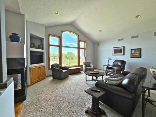 Light-filled great room featuring vaulted ceilings, gas fireplace & large picture window w/expansive panoramic views of golf course