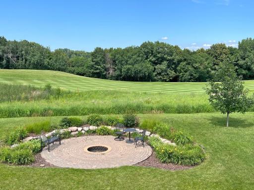 View out primary bedroom window of backyard firepit patio, rolling hills, and woods