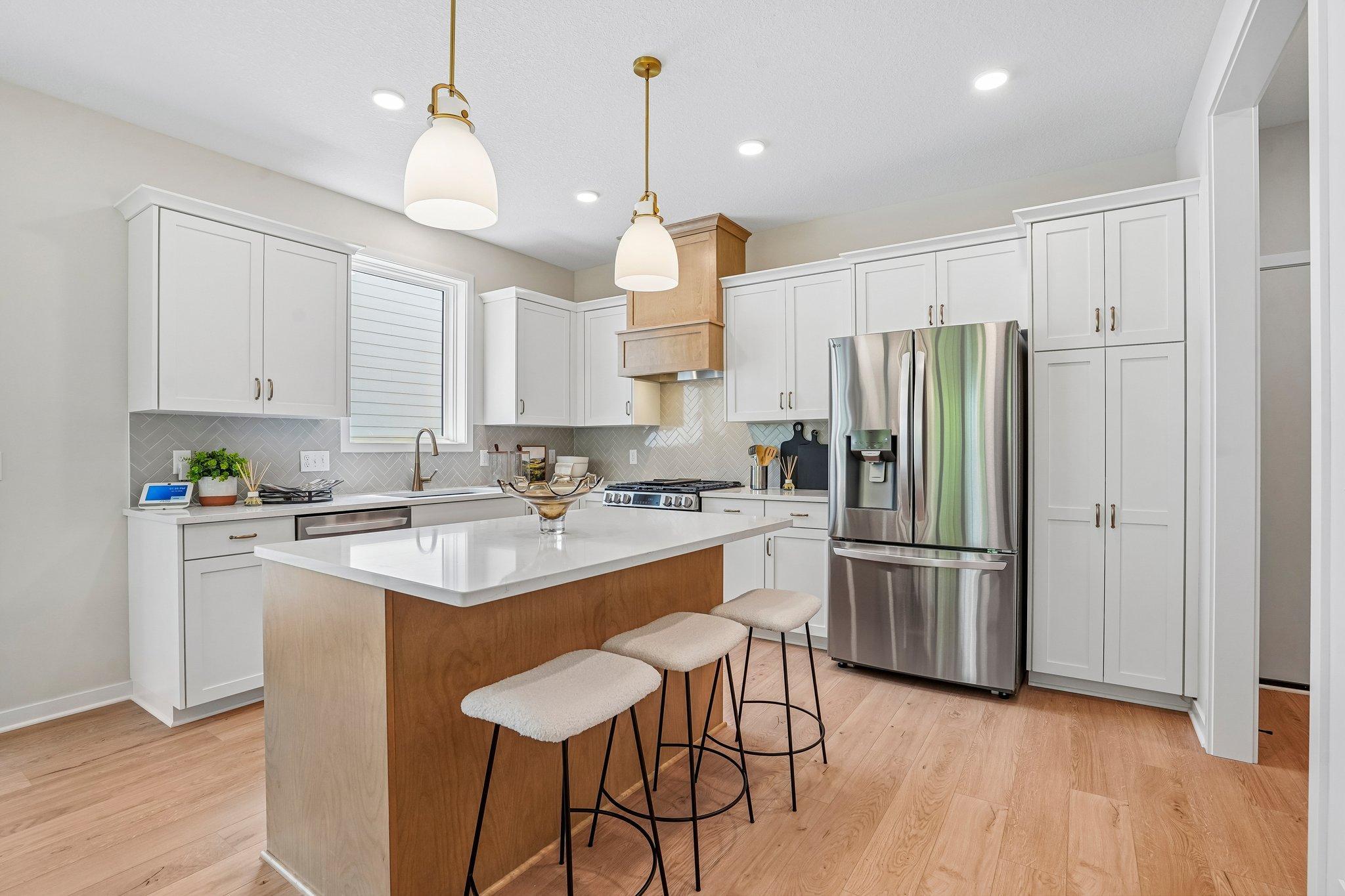Gourmet kitchen design showcases painted white cabinetry, stained wood hood and island, herringbone backsplash and marble-look quartz countertops.