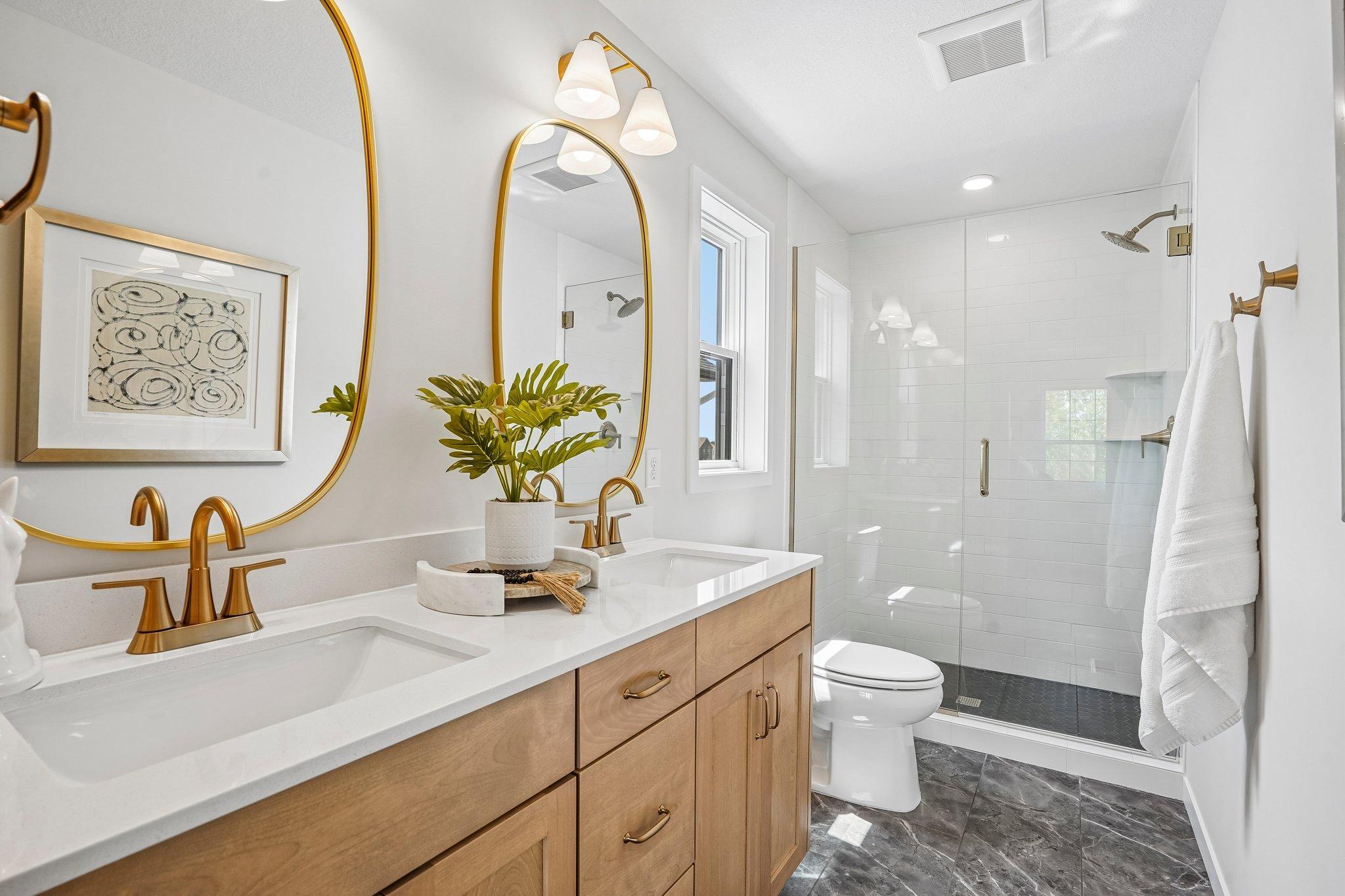 Luxurious primary suite is a tranquil retreat with spacious walk-in closet, ensuite bathroom, dual vanities, and ceramic tile shower and heavy glass door.