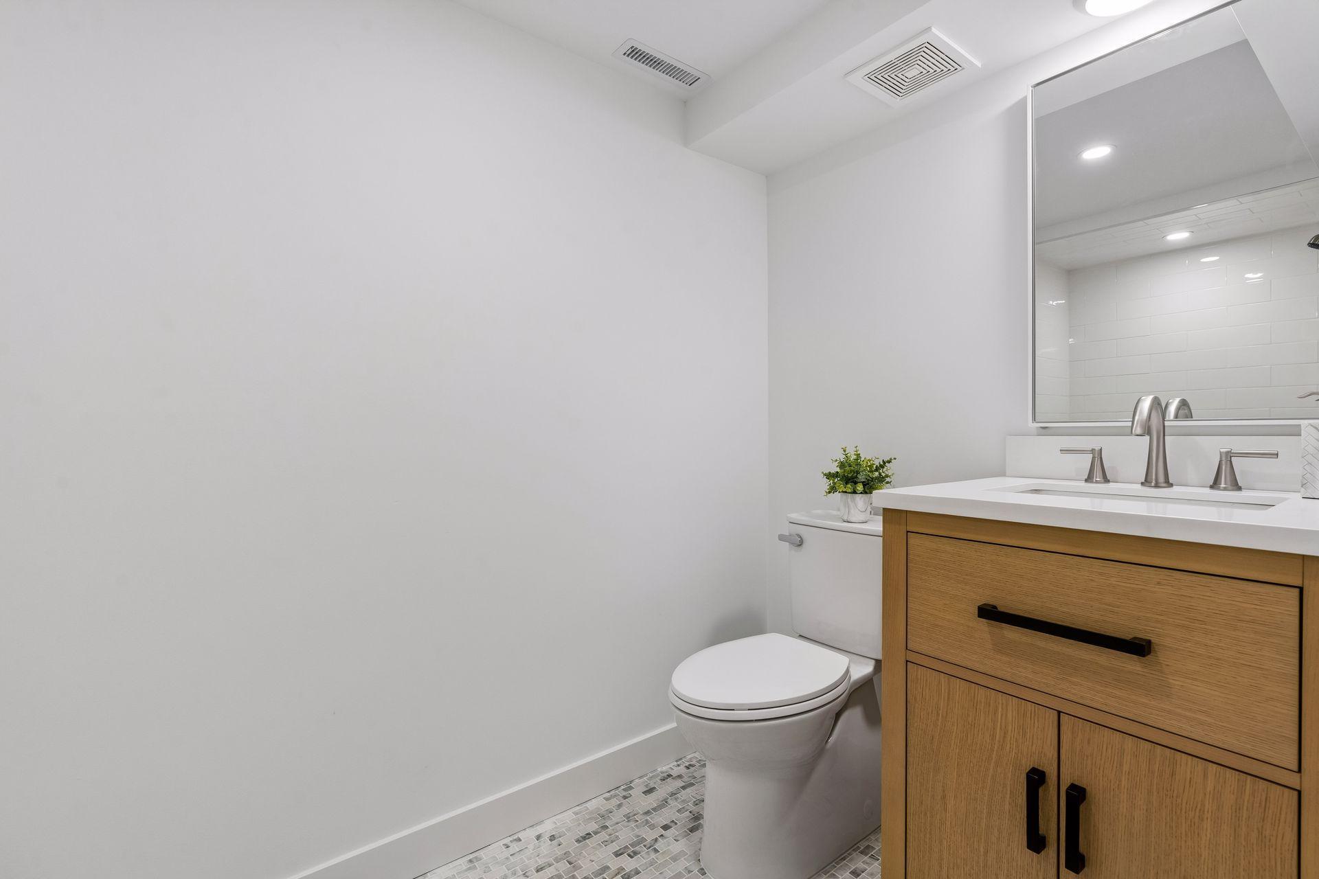 Lower Level 3/4 bathroom with updated Subway tile shower, White oak vanity with quartz top and Room and Board Mirror, New toilet, New lighting, and Marble flooring
