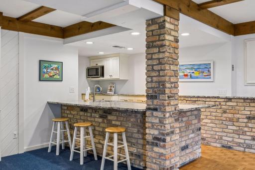 Entertain with ease in the lower-level second kitchen, featuring a refrigerator, brick accents, a prep sink, microwave, and generous counter seating